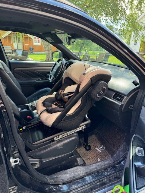 Axkid One 2 i brick melange, beige, i forsetet i en bil hos Holm Barnesikring, med mye benplass.
